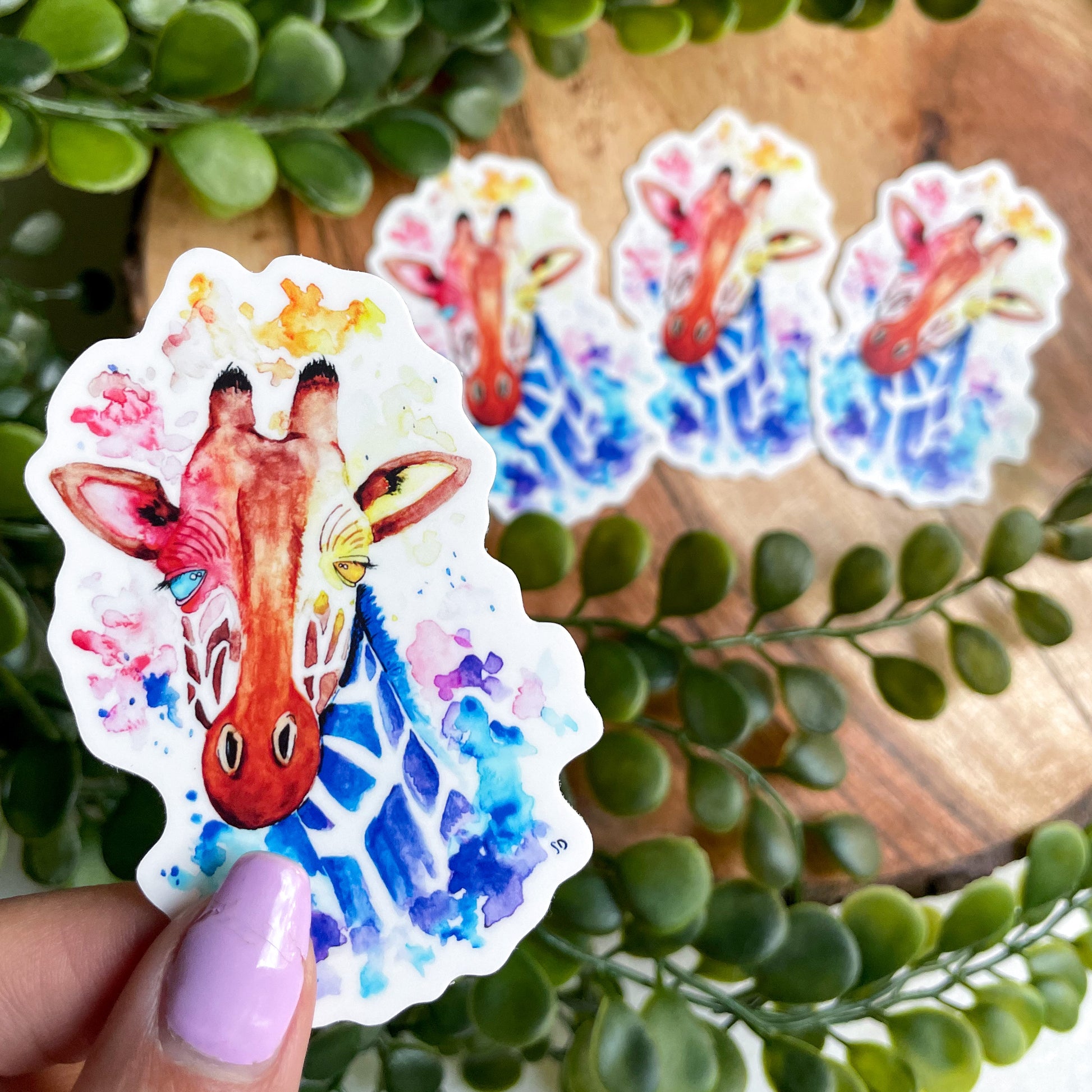 A close-up image of the waterproof, vinyl, dye-cut sticker depicting a watercolor painting from the Wild Planet Creations wild animal collection of a giraffe.