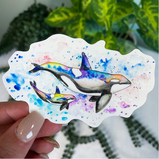 A close-up image of the waterproof, vinyl, dye-cut sticker depicting a watercolor painting from the Wild Planet Creations wild animal collection of rainbow orcas (mother and calf).